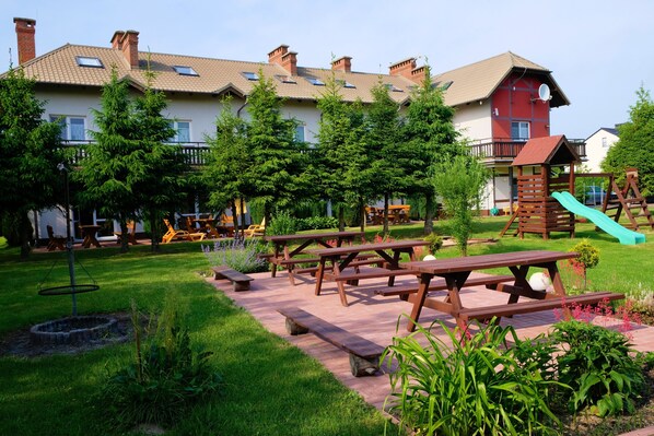 A courtyard with picnic tables, playground equipment, and a building with a red facade.