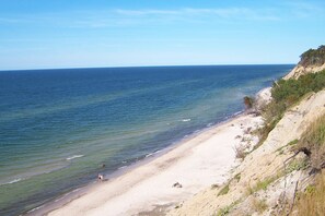 A beach with clear blue water, sandy shore, and a rocky cliff.