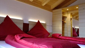 Un dormitorio con techo de madera, cama con ropa de cama roja y un espejo que refleja parte de la habitación.
