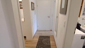 Un couloir avec un plancher en bois, des murs blancs et une porte au fond.