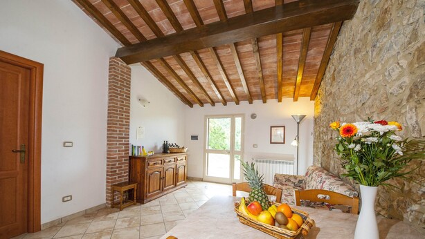 A kitchen with a tiled floor, wooden ceiling beams, a brick wall, and a dining area with a table set with fruit and a vase of flowers. - Panorama-Ferien-Toscana
Your vacation home in Tuscany (massa marittima)