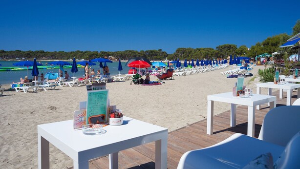 A beachside restaurant with outdoor seating, a menu board, and beach umbrellas. - Apartment Ema (Ližnjan)