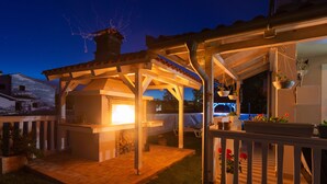 An outdoor patio area with a pergola, a barbecue grill, and hanging planters. - Apartment Ema (Ližnjan)