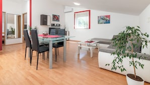A modern living room with a glass dining table, black chairs, a white sofa, a potted plant, and artwork on the walls. - Apartment Ema (Ližnjan)