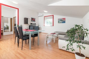 A modern living room with a glass dining table, black chairs, a white sofa, a potted plant, and artwork on the walls.