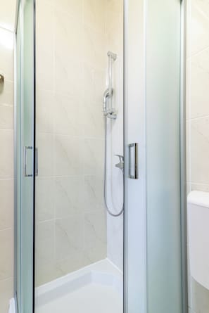 A glass-enclosed shower with a handheld showerhead and a wall-mounted faucet.