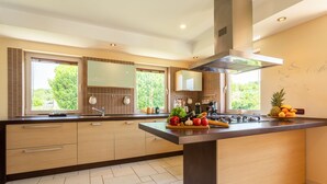 Een moderne keuken met een groot kookeiland, houten kasten en uitzicht op groen.