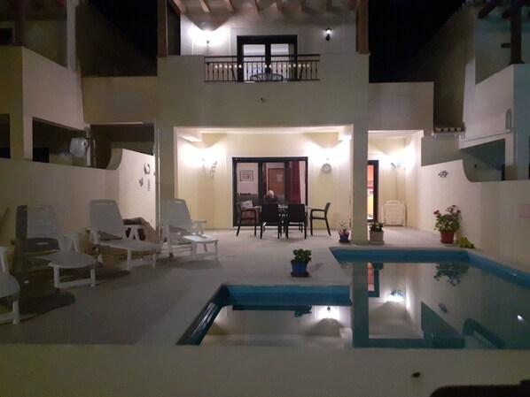 A two-story building with a pool, lounge chairs, and a dining area.