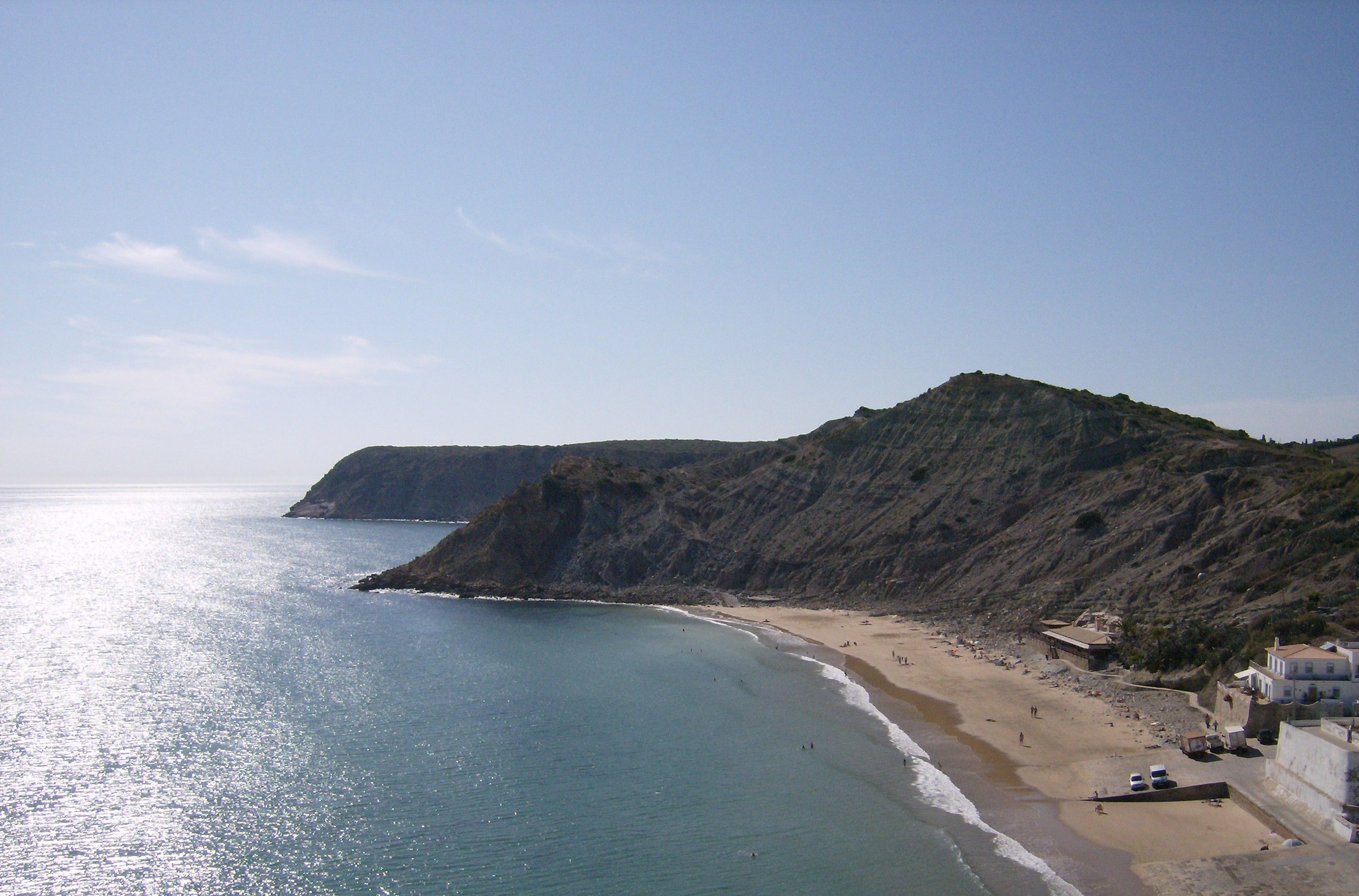 A coastal landscape with a beach, cliffs, and a clear sky.