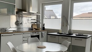 Cozinha moderna com armários brancos, exaustor de aço inoxidável e área de jantar com mesa redonda e cadeiras brancas.