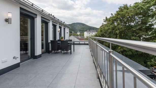 A balcony with a table and chairs, a metal railing, and a view of a mountain and trees.