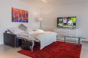 A modern hotel room with a bed, a red rug, a glass table, a TV, and a painting on the wall. - Vis-Ahr-Vis Penthouse (Bad Neuenahr)