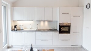 A modern kitchen with white cabinets, a black oven, and a dining area with a wooden table set for two.