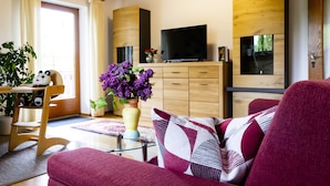 A modern living room with a sofa, a TV, wooden cabinets, and a dining area with a table and chairs. - Arrive, switch off ... feel good (Aidenbach)