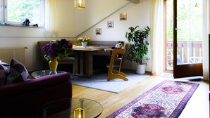 A cozy living room with a sofa, a glass coffee table, a dining table with chairs, a potted plant, and a view through a sliding glass door. - Arrive, switch off ... feel good (Aidenbach)