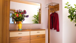A bathroom with a wooden vanity, a mirror, a vase with flowers, and a coat rack with a red coat. - Arrive, switch off ... feel good (Aidenbach)