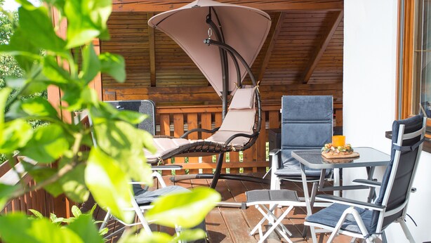 A wooden deck with outdoor furniture including a swing chair, two lounge chairs, and a table with a fruit bowl. - Arrive, switch off ... feel good (Aidenbach)