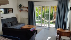 Ein modernes Wohnzimmer mit einer Couch, einem Couchtisch, einem Fernseher und einem Balkon mit Vorhängen.