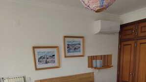 Ein Schlafzimmer mit einem Bett, einem hölzernen Kopfteil, zwei gerahmten Bildern, einem Nachttisch, einer Lampe und einem Kleiderschrank.