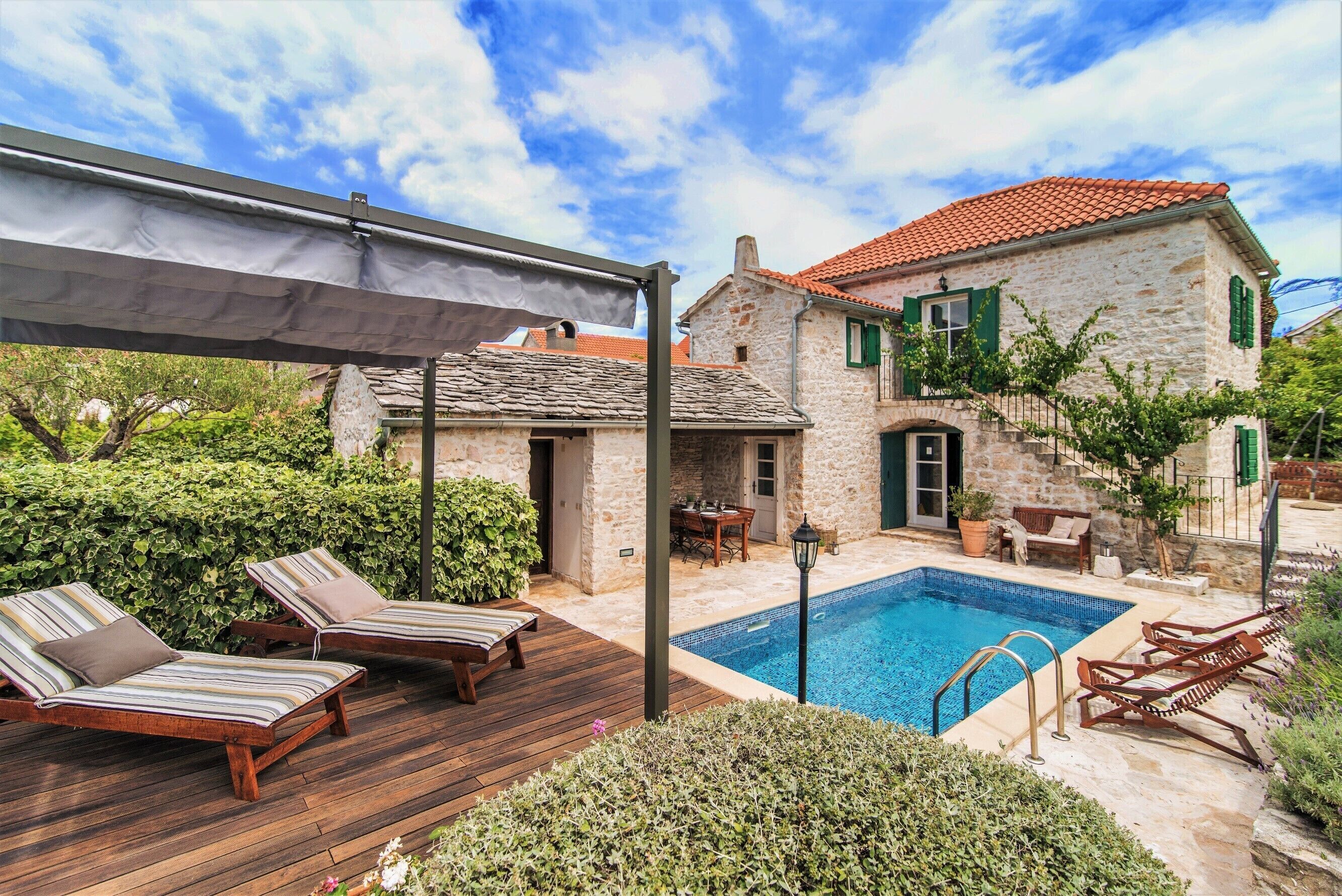 A stone house with a swimming pool, wooden deck, and lounge chairs.