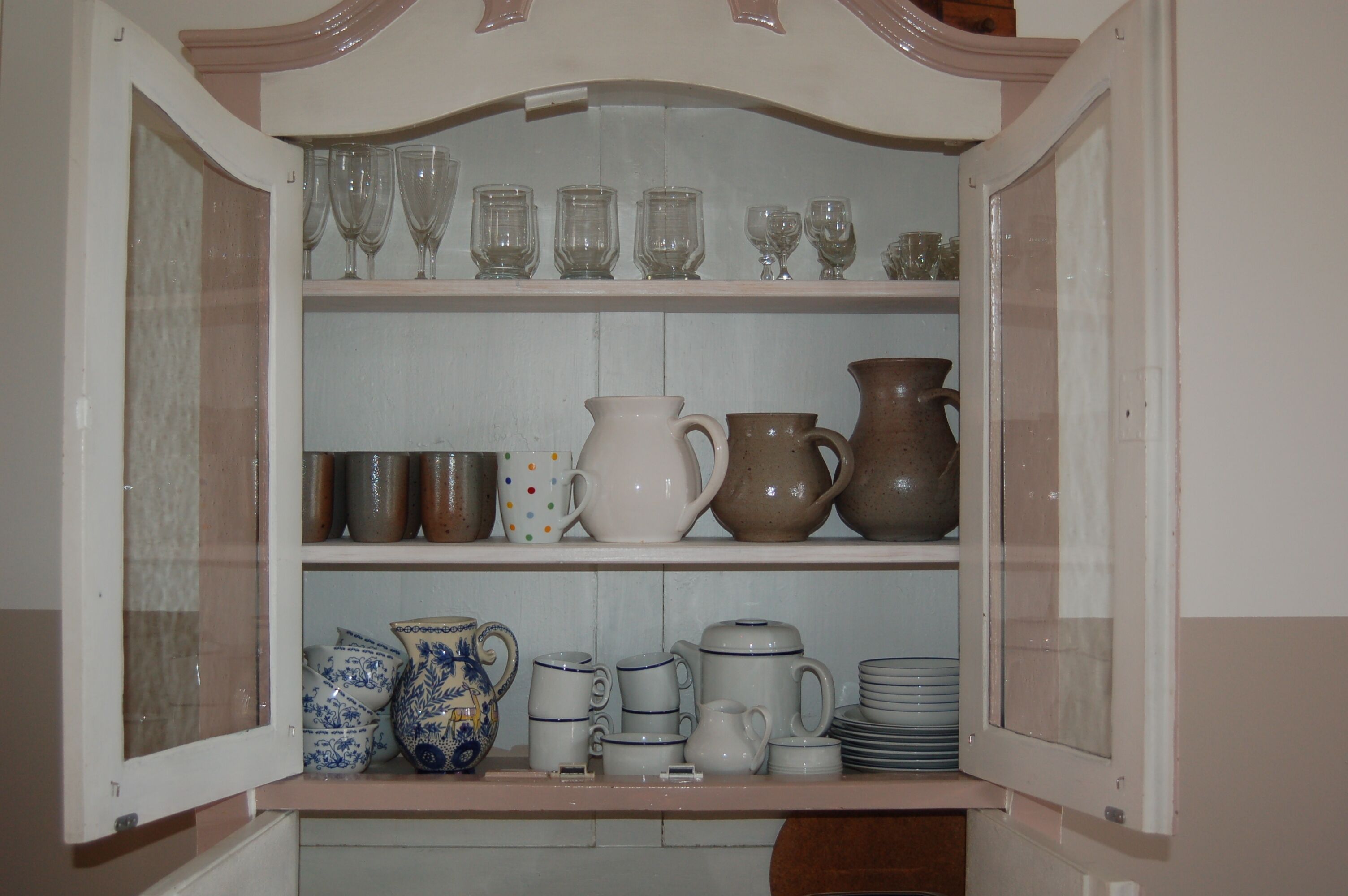 A cabinet with shelves containing various glassware, ceramic mugs, and plates.