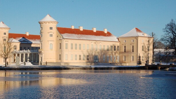 Een groot, historisch gebouw met een centrale toren en meerdere vleugels, gelegen aan een bevroren waterlichaam.