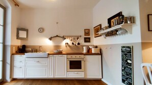 Een keuken met witte kastjes, een spoelbak, een fornuis en een klok aan de muur.