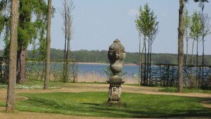 Een tuin met een stenen urn, bomen en een meer op de achtergrond.