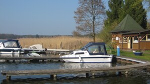 Een jachthaven met aanmerende boten, een houten gebouw met een groen dak, en een boom op de achtergrond.