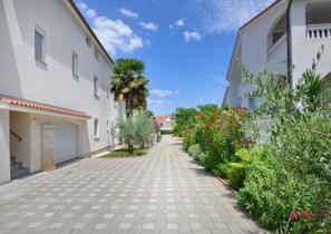 A residential street with white buildings, a paved walkway, and greenery.