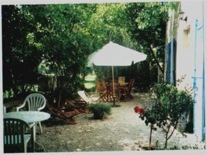 An outdoor seating area with a table and chairs, a white umbrella, and a gravel path. - Charming character home in the hills above Aix--------------------- (Aix-En-Provence)