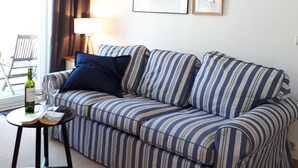 A striped sofa with a small side table, a framed picture, and a window with curtains. - Close to the beach, comfortable apartment in a very good location! (Kühlungsborn Ost)