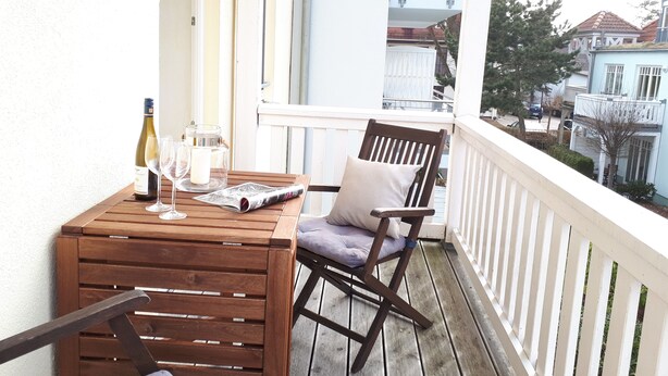 A wooden table with a bottle of wine, glasses, and a candle on a balcony with white railings. - Close to the beach, comfortable apartment in a very good location! (Kühlungsborn Ost)