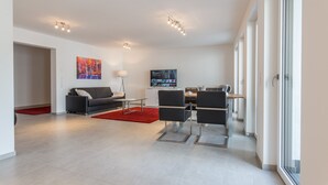 Ein modernes Wohnzimmer mit einer Couch, Sesseln, einem Couchtisch und einem Fernseher.