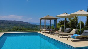A swimming pool with lounge chairs and umbrellas, overlooking a scenic landscape. - Villa Harmony, fantastic view, pool 12 m, cozy natural stone villa (Rethymno)