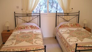 A bedroom with two single beds, each with a floral-patterned bedspread, a nightstand with a lamp, and a window with curtains.