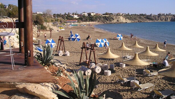 A beach with umbrellas, lounge chairs, and a wooden structure.