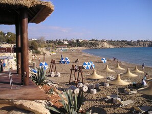 A beach with umbrellas, lounge chairs, and a wooden structure. - 3-bedroom poolside villa in Kato Paphos, Cyprus with roof terrace and free Wi-Fi (Paphos)