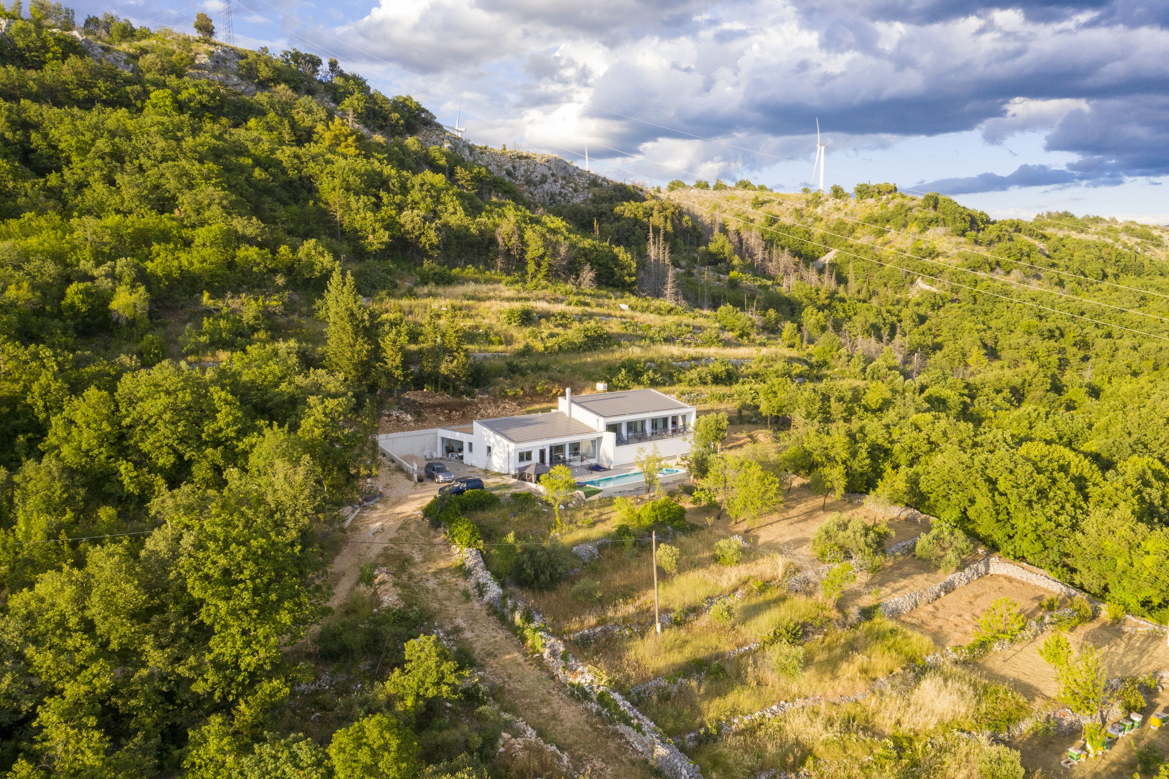 Une maison moderne dotée d’une piscine, entourée d’une végétation luxuriante et de collines.