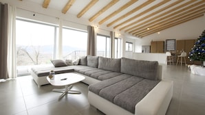 A modern living room with a sectional sofa, a white coffee table, and a view of the mountains through large windows.