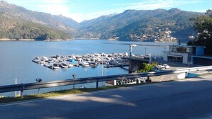 Un puerto deportivo con barcos amarrados, una carretera con barandilla y montañas al fondo.