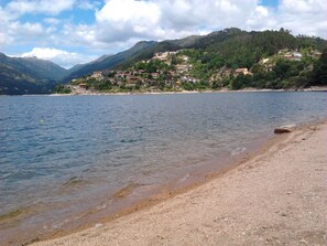 A lakeside view with a sandy beach, a calm lake, and a hillside with buildings. - Geres - Vacation / Weekends (Gerês)