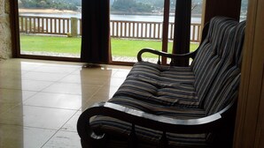 Habitación con vistas a un lago y colinas. Cuenta con un sofá a rayas y una barandilla de madera.