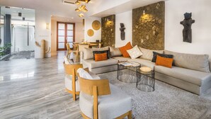 A modern living room with a large sofa, two armchairs, a coffee table, and a dining area with a table and chairs.