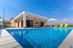 Un área moderna junto a la piscina con una piscina azul cristalina, tumbonas y una zona de estar cubierta.