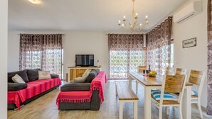 Een woonkamer met een bank, een televisie, een eettafel met stoelen en een kroonluchter.