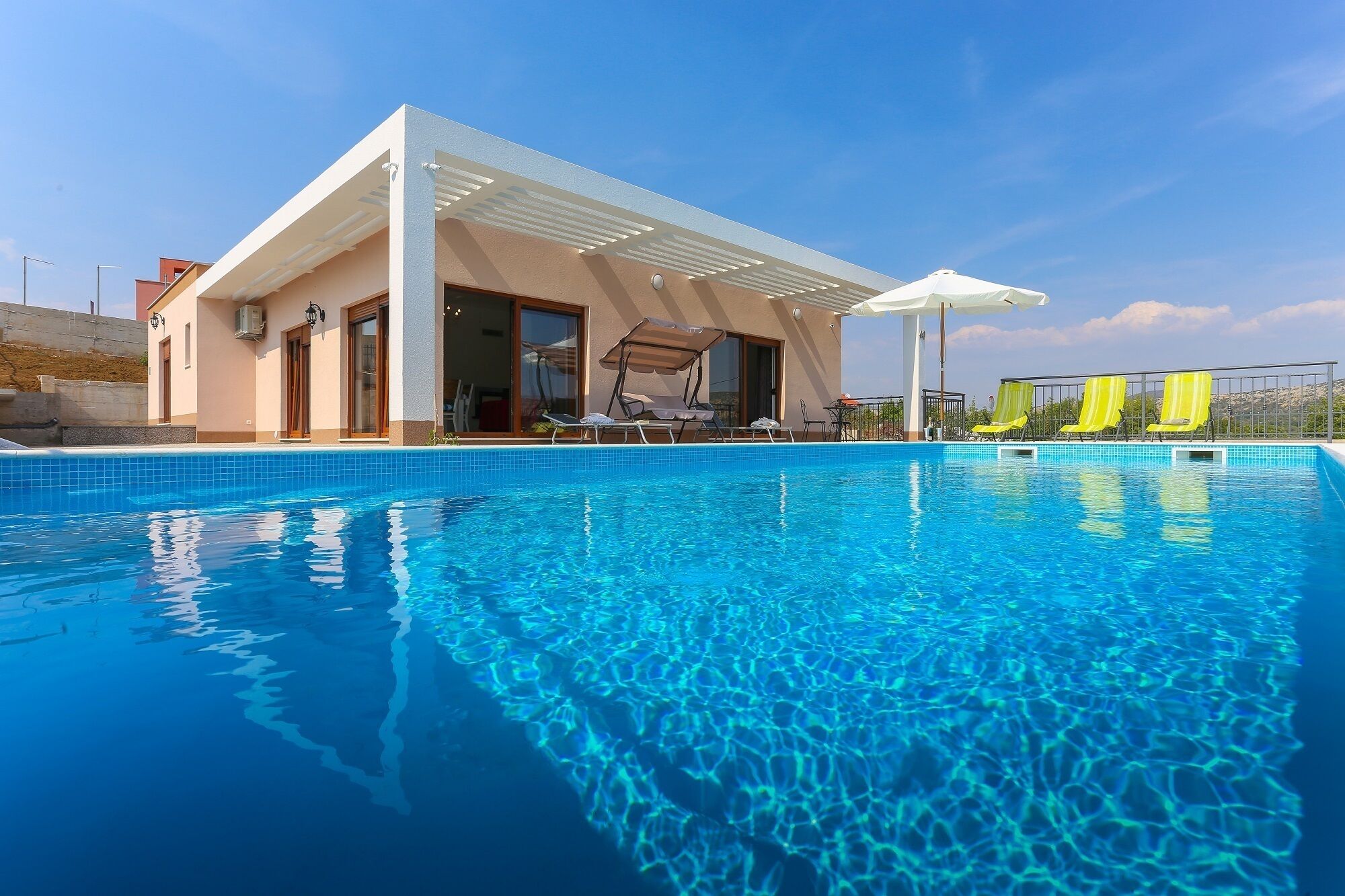 A modern pool area with clear blue water, a covered seating area, and yellow lounge chairs.
