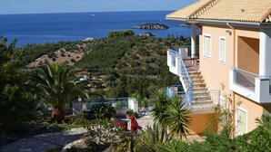 A coastal building with a balcony, a paved pathway, and a view of the sea. - Villa Orea Thea with pool, German standard for up to 6 people (Syvota)