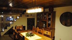 Un espace repas comprenant une table en bois, des chaises, un lustre, un mur en pierre et un escalier.