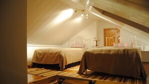 Une chambre mansardée chaleureuse avec deux lits, un plancher en bois et un plafond en pente doté de fenêtres de toit.